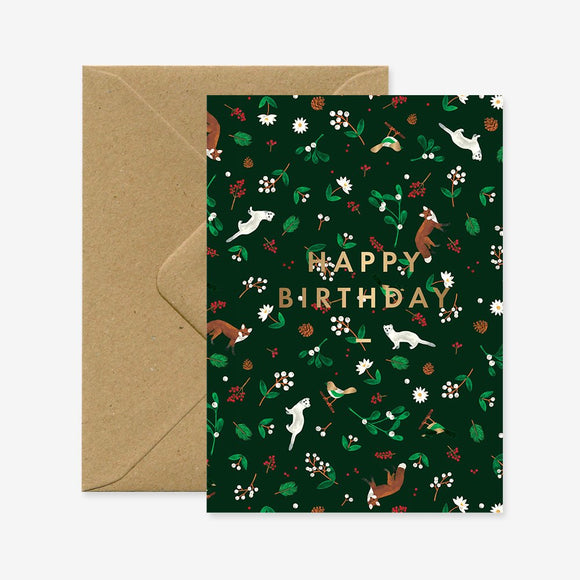 A birthday greeting card with a green floral pattern and gold foil details, displaying the text 'Happy Birthday'. It is accompanied by a brown envelope.