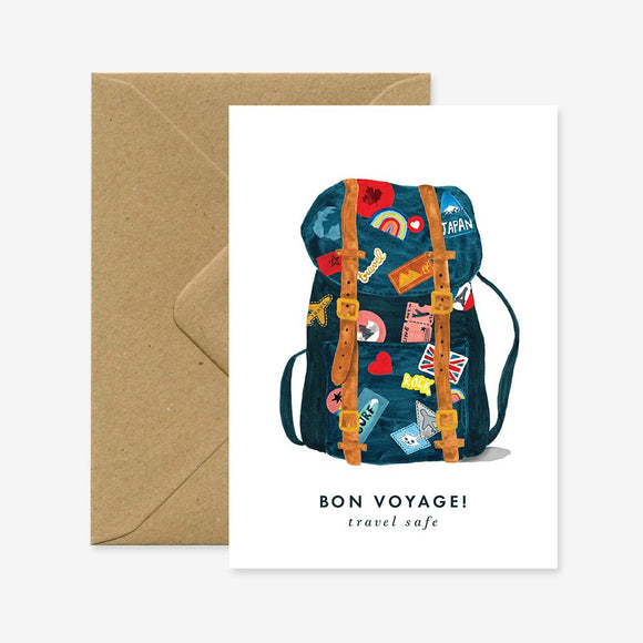 A greeting card with a illustration of a backpack with travel stickers and the text 'BON VOYAGE! travel safe' on it. There is a brown envelope behind the card.