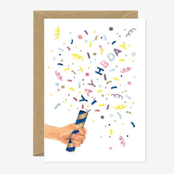 A birthday greeting card with a colorful illustration of a party popper with the words 'YAY HBDAY' and various confetti patterns coming out of it. The card is accompanied by a brown envelope.