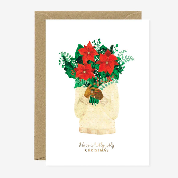 A Christmas greeting card featuring a watercolor illustration of poinsettias in a vase, with gold foil details and the text 'Have a holly jolly Christmas'. A brown envelope is included.