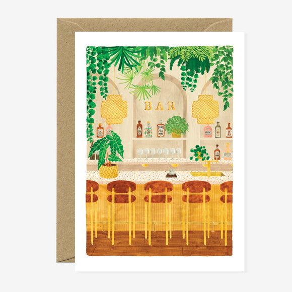 Illustrated greeting card depicting a bar scene with greenery, stools, and bottles, blank interior, gold foil details, and a brown envelope.