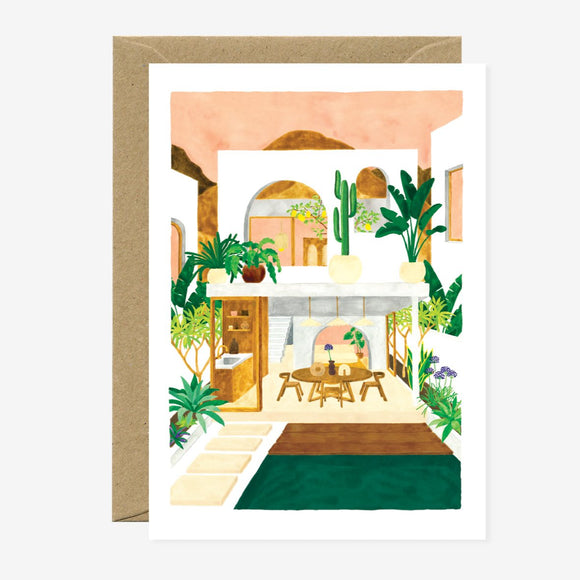 A greeting card featuring an illustration of an interior space with plants and a wooden table, accompanied by a brown envelope.