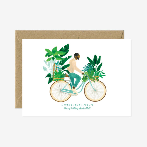 A birthday greeting card with a illustration of a person on a bicycle surrounded by plants, with a gold foil detail and a brown envelope.