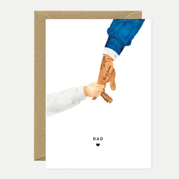 A greeting card with an illustration of two hands reaching towards each other, with the word 'DAD' written on the forearm of one hand, and a brown envelope in the background.