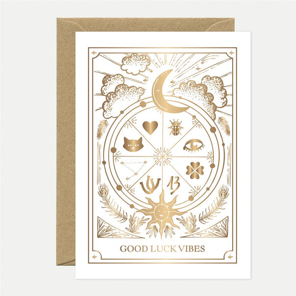 A white greeting card with gold foil designs and text that reads 'GOOD LUCK VIBES', accompanied by a brown envelope.