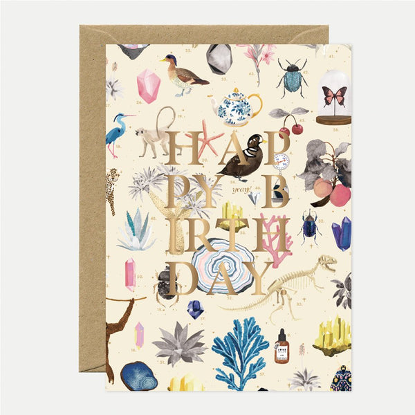 A birthday greeting card with gold foil details, featuring a variety of illustrations such as birds, insects, and plants, accompanied by a brown envelope.