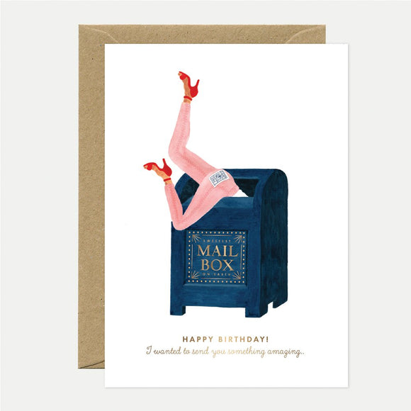 A greeting card with an illustration of a person's legs sticking out of a blue mailbox, with gold foil details and text that reads 'Happy Birthday! I wanted to wish you something amazing.'.