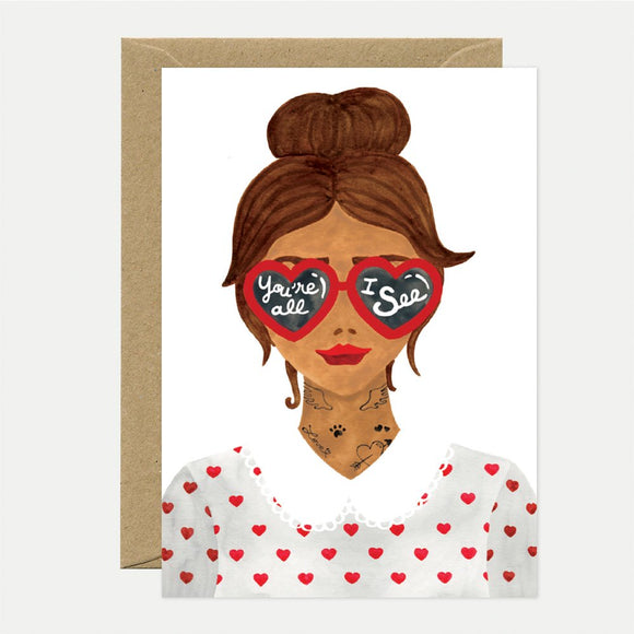 A greeting card with an illustration of a character wearing heart-shaped sunglasses with the words 'You're All I See' and 'I Said' on them. The card is accompanied by a brown envelope.