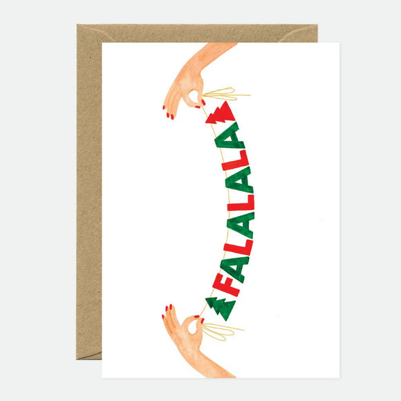 A Christmas greeting card with 'FALALALA' written in stylized text, accompanied by two hands making peace signs. The card is accompanied by a brown envelope.