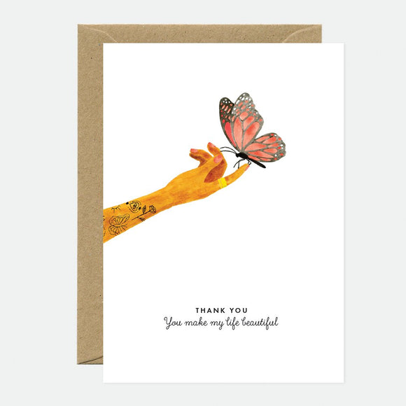 A thank you greeting card with a butterfly sitting on a hand, with a brown envelope.