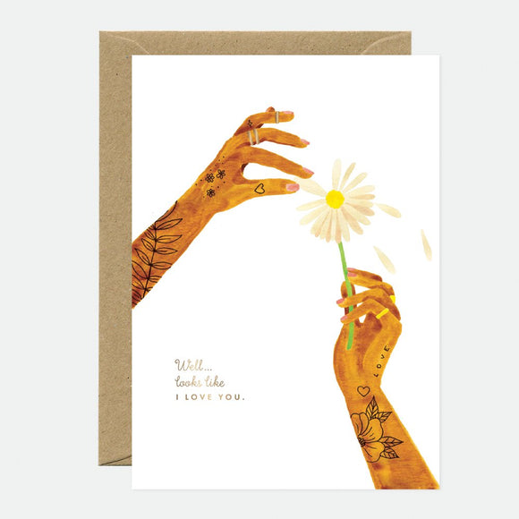 A greeting card with an illustration of hands offering a daisy flower, with gold foil details and the text 'I love you'. It comes with a brown envelope.
