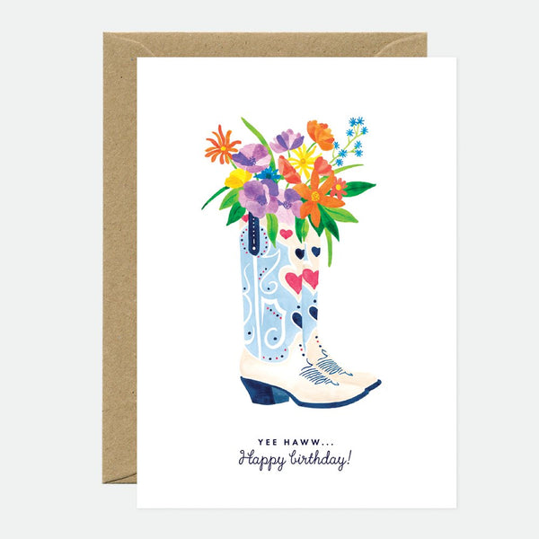 A birthday greeting card with a floral design in a boot, with a 'Happy Birthday' text, presented with a brown envelope.