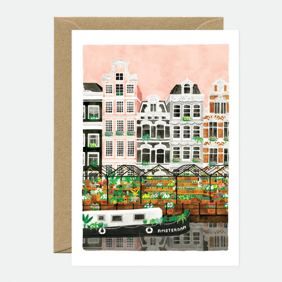 A greeting card featuring an illustration of Amsterdam's cityscape with colorful buildings and a canal, accompanied by a recycled brown envelope.