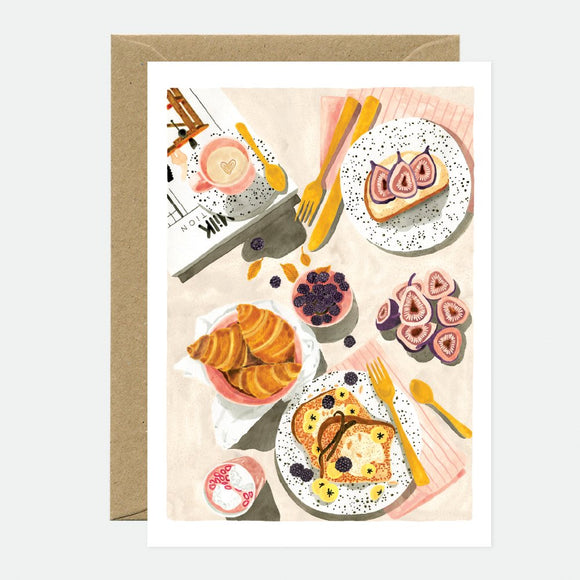 A greeting card with an illustration of a brunch spread including pancakes, eggs, and smoked salmon on plates, accompanied by a brown envelope.