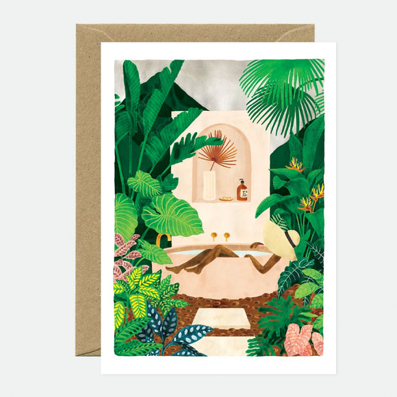 A greeting card depicting a bathtub surrounded by lush greenery, with gold foil details and a brown envelope.