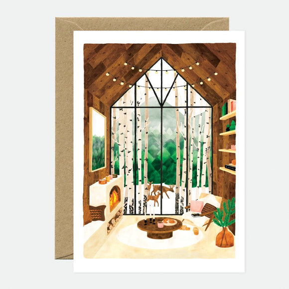 A greeting card depicting a cozy indoor scene with a fireplace, bookshelves, and a view of a snowy landscape through large windows.