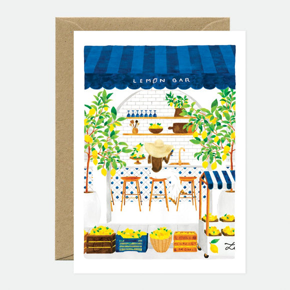 A greeting card featuring an illustration of a lemon bar stand with blue awnings, yellow lemons, and green plants. There is a brown envelope included.