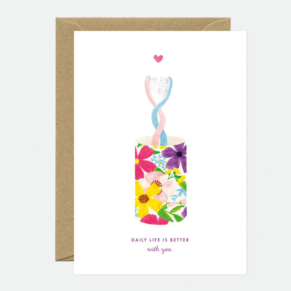 A greeting card with a floral design and a heart, with a blank interior, accompanied by a brown envelope.