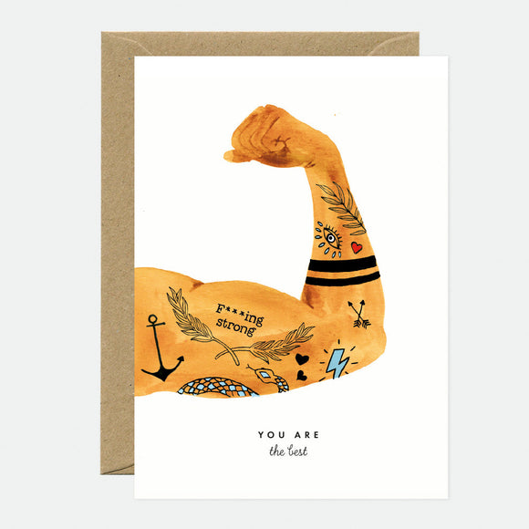A greeting card with an illustration of a tattooed arm flexing, with words 'Prove yourself strong' and an anchor tattoo, and a brown envelope. The text on the card reads 'YOU ARE the best'.