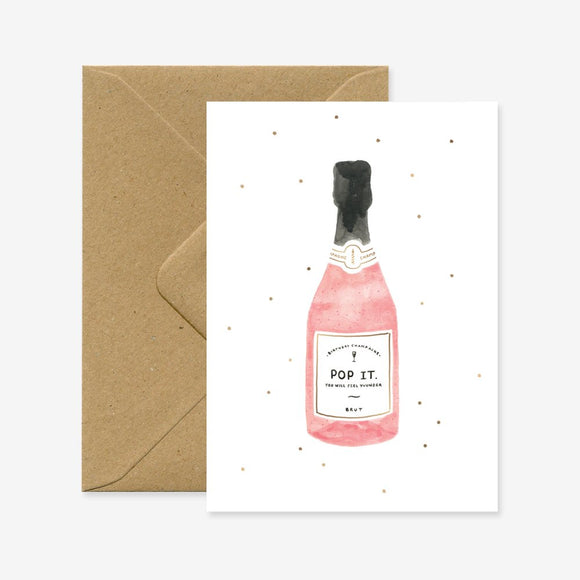 A birthday greeting card with a illustration of a pink champagne bottle and the text 'POP IT'. The card is accompanied by a brown envelope.
