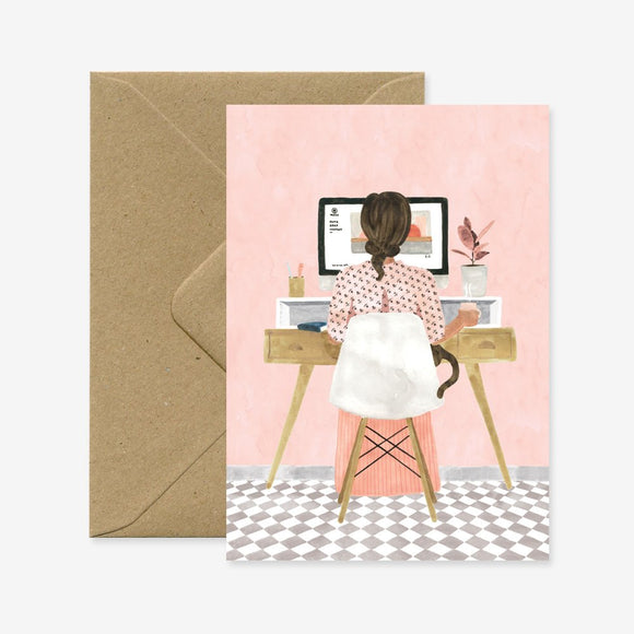 A greeting card depicting a cartoon illustration of a woman sitting at a desk with a computer, with a brown envelope in the background.