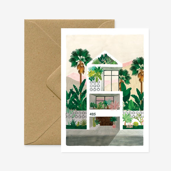 A greeting card with an illustration of a house surrounded by plants, accompanied by a brown envelope.
