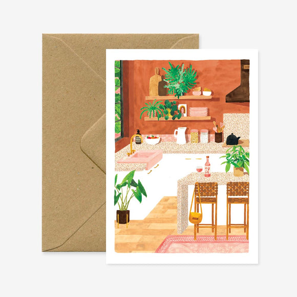 A greeting card depicting a colorful illustration of a kitchen scene, accompanied by a recycled brown envelope.