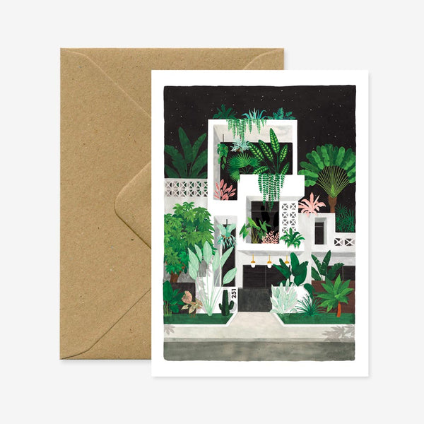 A greeting card with an illustration of a night scene with buildings and plants, accompanied by a brown envelope.