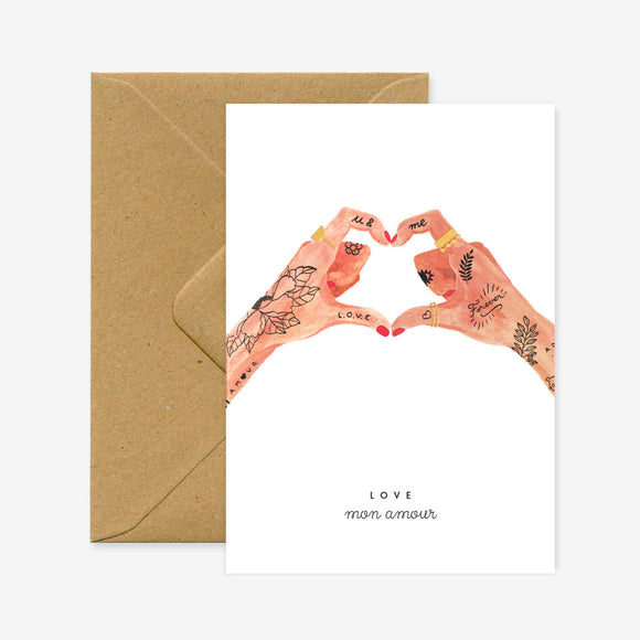 A greeting card with a design of hands forming a heart shape and the word 'LOVE' printed at the bottom, accompanied by a brown envelope.