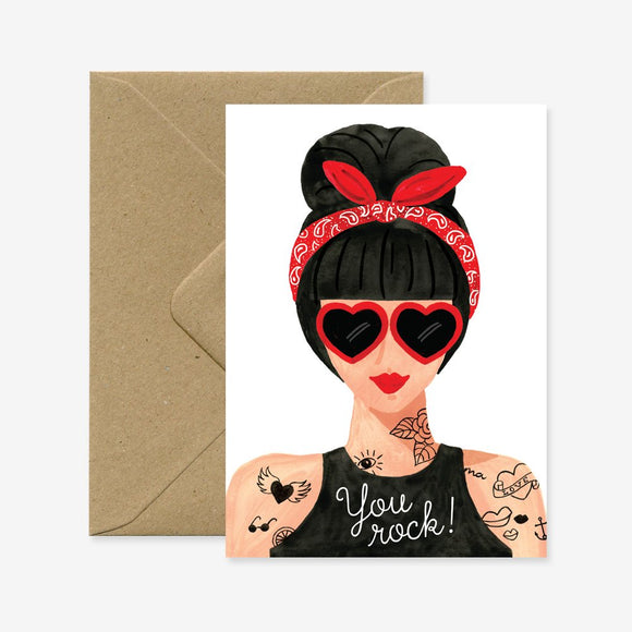 A greeting card with an illustration of a stylized woman with a red bandana and heart-shaped sunglasses, accompanied by the text 'You rock!' and a brown envelope.