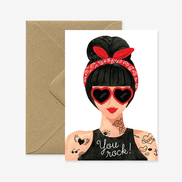 A greeting card with an illustration of a stylized woman with a red bandana and heart-shaped sunglasses, accompanied by the text 'You rock!' and a brown envelope.
