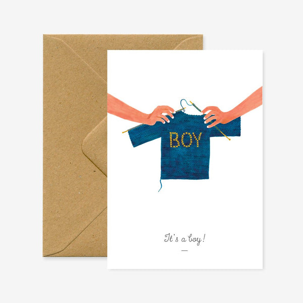 A greeting card with an illustration of a onesie with the word 'BOY' on it, and a brown envelope.