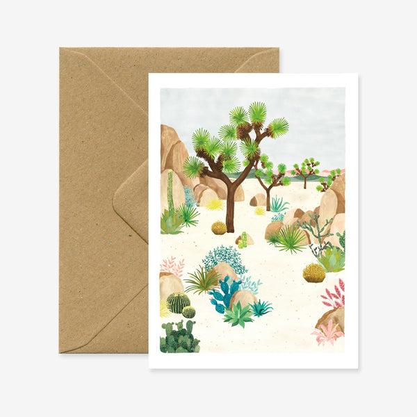 A greeting card with an illustration of a desert landscape, featuring Joshua trees and other plants, accompanied by a brown envelope.