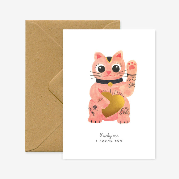 A greeting card featuring a illustration of a lucky cat with gold foil details, accompanied by a brown envelope.