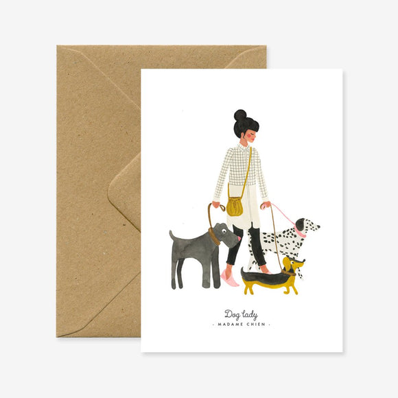A greeting card with an illustration of a woman with three dogs, accompanied by a brown envelope.