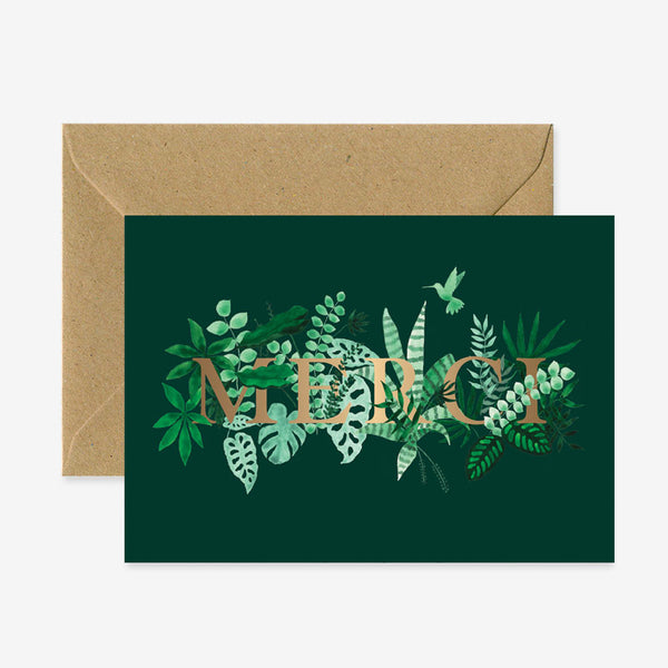 A green greeting card with a floral pattern and the word 'MERCI' in bold letters, accompanied by a brown envelope.