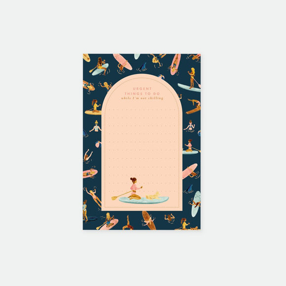 A notepad with a water-inspired design featuring paddleboarding girls. The notepad has a peach-colored cover with a semi-circular cut-out revealing part of the design inside.