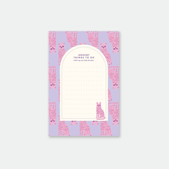 A notepad with a playful design featuring a stinky cat on a purple background with pink dots and a pattern of cats around the edges.