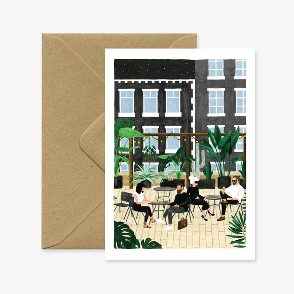 A greeting card depicting a rooftop cafe scene with people seated at tables, accompanied by a brown envelope.