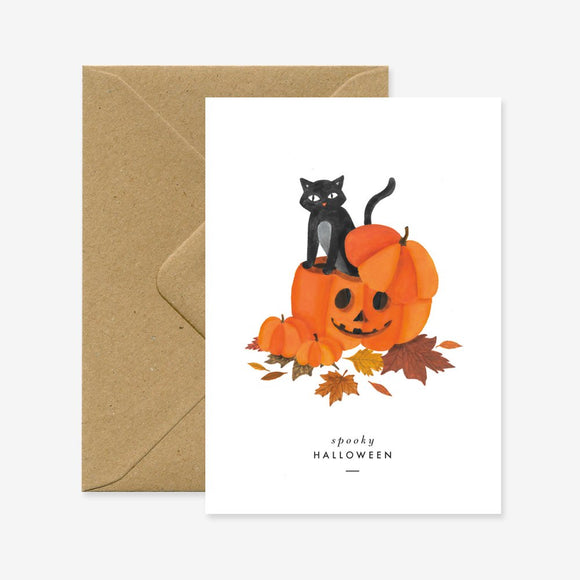A greeting card with a Halloween theme, depicting a black cat sitting on top of a pumpkin, surrounded by autumn leaves. The text on the card reads 'Spooky Halloween'.
