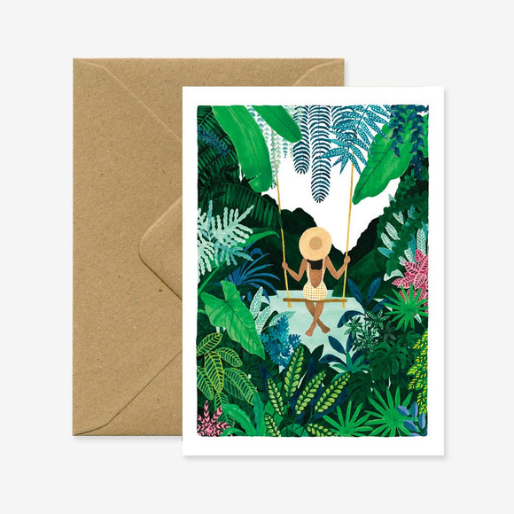 A greeting card with an illustration of a person sitting on a swing in a lush green jungle, accompanied by a brown envelope.