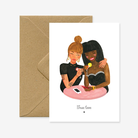 A greeting card with an illustration of two people sitting close and sharing a moment, with the text 'True love' at the bottom. There is a brown envelope behind the card.
