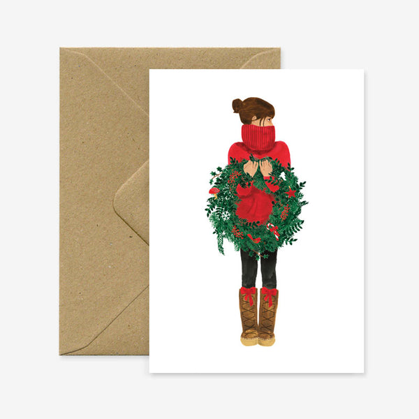 A Christmas greeting card featuring an illustration of a girl with a wreath, accompanied by a brown envelope.