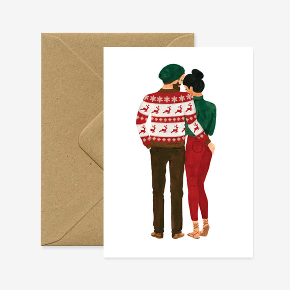 A Christmas greeting card depicting a couple from behind, wearing holiday-themed clothing, with a brown envelope.