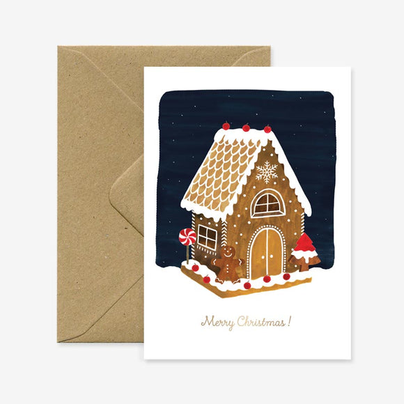 A Christmas greeting card with a illustration of a gingerbread house on the front, with a brown envelope. The text on the card reads 'Merry Christmas!'.