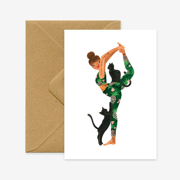 A greeting card with an illustration of a yoga pose, accompanied by a black cat, on a natural white paper. The card is accompanied by a recycled brown envelope.