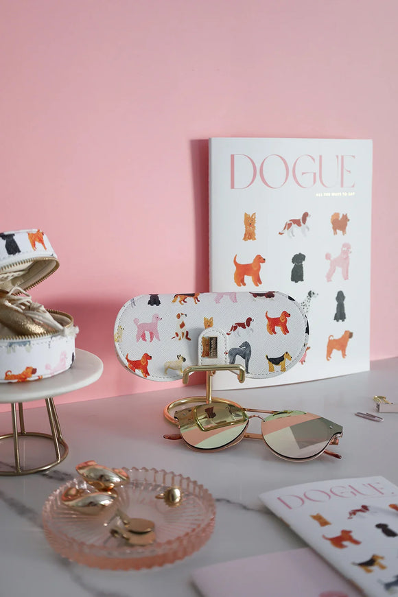 Dog-pattern glasses case styled with sunglasses, jewelry tray, and Dogue stationery on a marble table.