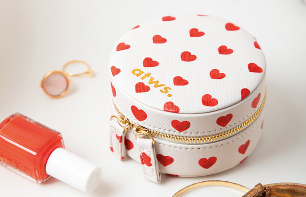 A round white travel jewelry box adorned with a red heart pattern and a gold embossed All the Ways to Say logo, perfect for organizing small accessories.