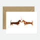 A greeting card with an illustration of two dachshunds kissing, accompanied by a recycled brown envelope.