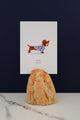 All The Ways To Say Oui Oui Merci card – dachshund in striped shirt holding baguette, styled with bread and marble backdrop